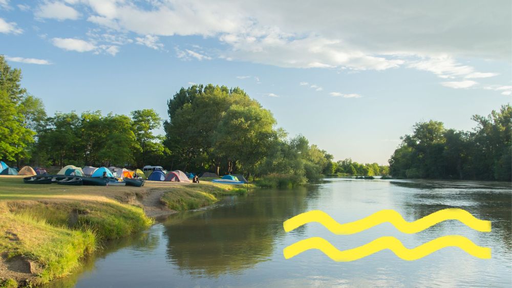 Eine Gruppe Zelte auf einer Wiese am Fluss bei schönem Wetter.