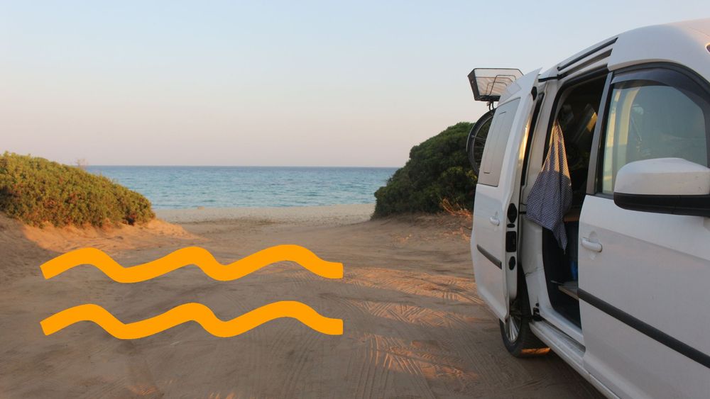 Ein Caddy steht im Abendlicht mit offener Heckklappe auf einem Sandstrand am Meer.